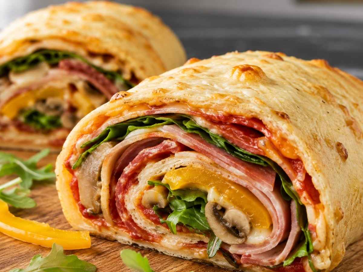 Angeschnittenes Stück Low-Carb-Pizzarolle mit Käsefüllung und Rucola in Nahaufnahme