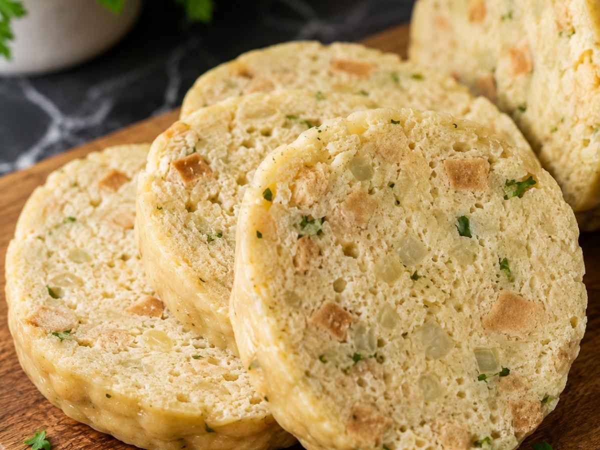 Nahaufnahme einer Serviettenknödel-Scheibe mit weicher, pudding-artiger Konsistenz und sichtbaren Kräutern