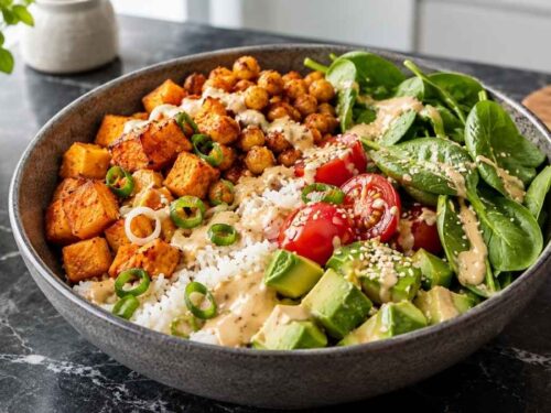 Vegane Süßkartoffel-Bowl mit Kichererbsen, Reis, Avocado und Tahin-Sauce in einer Schüssel von oben