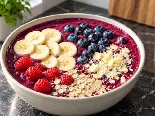 Zwei Schalen Blaubeer-Bananen-Bowl mit frischen Beeren, Bananenscheiben, Haferflocken und weißen Schokoraspeln auf einem hellen Tisch